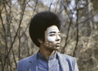 Kimyan Law / Kulturforum Prag Das Bild zeigt das Gesicht und den Oberkörper des Künstlers, er steht vor der Kamera und blickt nach links in die Gerne. Sein Gesicht ist mit weißer Farbe bemalt.