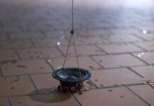 Ada Kobusiewicz & Christian F. Schiller / Kulturforum Warschau Das Bild zeigt ein Fragment einer Installation, einen Teil eines Lautsprechers, der an einem Kupferkabel direkt über dem Boden hängt, umgeben von vielen kleinen Kupfermünzen, die vom Magnetfeld angezogen werden.