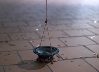 Ada Kobusiewicz & Christian F. Schiller / Kulturforum Warschau Das Bild zeigt ein Fragment einer Installation, einen Teil eines Lautsprechers, der an einem Kupferkabel direkt über dem Boden hängt, umgeben von vielen kleinen Kupfermünzen, die vom Magnetfeld angezogen werden.