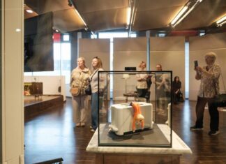 Ausstellung „Judith Lava: Darf ich vorstellen – Lili!“ / Kulturforum Bratislava Auf dem Bild sieht man in einer Vitrine einen Toaster, aus dem die kleine Lilly raushängt. Die Besucherinnen der Ausstellung sehen es sich an.