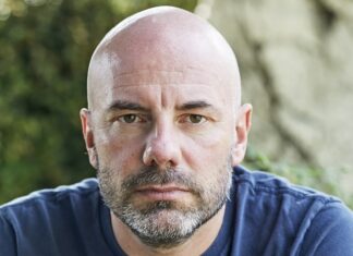 Lesungen mit Daniel Wisser/ Kulturforum Ljubljana Das Bild zeigt Daniel Wisser. Er trägt ein blaues T-Shirt. Der Autor hat einen Drei-Tage-Bart und eine Glatze. Er blickt direkt in die Kamera und wirkt nachdenklich.