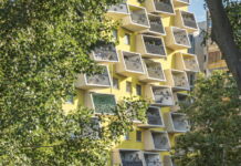 Architektur in Österreich / Kulturforum Rom Das Bild zeigt einen gelben Wohnblock der querkraft architekten mit kleinen Balkonen. Links und rechts ist das Gebäude von Blattwerk umgeben.