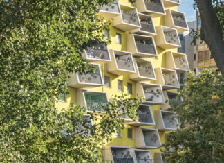 Architektur in Österreich / Kulturforum Rom Das Bild zeigt einen gelben Wohnblock der querkraft architekten mit kleinen Balkonen. Links und rechts ist das Gebäude von Blattwerk umgeben.