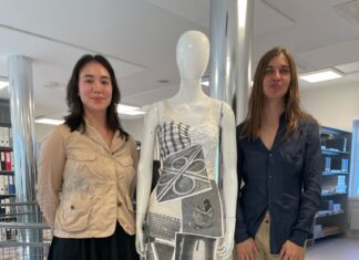 Something for Everyone, Everything for No One / Botschaft Oslo Das Foto wurde bei der Ausstellungseröffnung am 7.5.2025 aufgenommen und zeigt die beiden Künstlerinnen neben einem ihrer Werke. Links steht die US Künstlerin Teak RAMOS. Sie hat schwarze halblange Haare und dunkle Augen. Sie trägt einen schwarzen knielangen weiten Rock und eine beige Jacke, schwarze Strümpfe und Sneaker. Recht steht die österreichische Künstlerin Anna-Sophie BERGER. Sie hat hellbraune lange Haare und helle Augen. Sie trägt eine olivfarbene Hose, eine dunkelblaue Bluse und mit Strasssteinen besetzte schwarze Sandalen. In der Mitte steht ein Second Hand Mannequin das eine der Modeschöpfungen der beiden Künstlerinnen trägt. Ein beiges Leinenkleid, etwa knielang, das mit A4 Ausdrucken verschiedener schwarz-weiß Bilder aus der International Library of Fashion Research benäht ist. Darunter ein Kleeblatt-Autobahnknoten, eine sitzende nähende Frau und ein Schneidertisch.