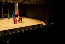 Duo Sonoma in Saudi-Arabien / Botschaft Riyadh Das Bild zeigt das Duo Sonoma auf einer Bühne, wie sie ihre Instrumente spielen. Hinter ihnen stehen die Flaggen von Saudi-Arabien, der EU und Österreich.