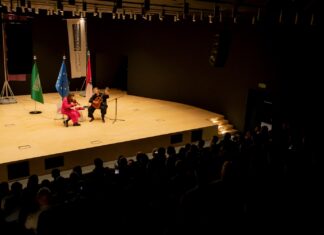 Duo Sonoma in Saudi-Arabien / Botschaft Riyadh Das Bild zeigt das Duo Sonoma auf einer Bühne, wie sie ihre Instrumente spielen. Hinter ihnen stehen die Flaggen von Saudi-Arabien, der EU und Österreich.