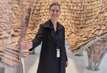 Kunst im Gespräch – Podcastserie Auf dem Bild steht Daniela Mitterberger vor einer Spiegelwand, in der ich Holzschindeln spiegeln.