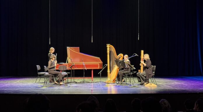 Bild: Fabian Schober Das Bild zeigt die Musikerinnen des Ensembles airborne extended bei einer Aufführung. Sie spielen verschiedene Instrumente wie Flöte, Harfe, Cembalo und Elektronik. Die Aufnahme ist in Schwarz-Weiß und zeigt eine konzentrierte Stimmung auf der Bühne.