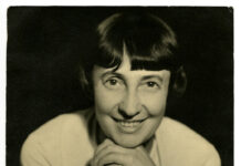 The Arc of History Lecture Series / Kulturforum London Das Bild zeigt Margarete Schütte-Lihotzky im Jahr 1935. Es handelt sich um eine schwarz-weiße Portraitaufnahme. Sie stützt ihr Kinn auf ihren Händen ab und lächelt direkt in die Kamera.