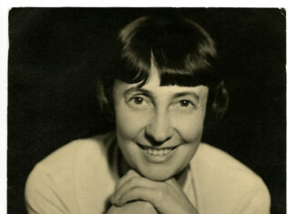 The Arc of History Lecture Series / Kulturforum London Das Bild zeigt Margarete Schütte-Lihotzky im Jahr 1935. Es handelt sich um eine schwarz-weiße Portraitaufnahme. Sie stützt ihr Kinn auf ihren Händen ab und lächelt direkt in die Kamera.