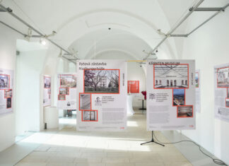 Bauherr:innenpreis 2022-2024 / Kulturforum Prag Das Bild zeigt die Galerie des Österreichischen Kulturforums. Auf beiden Seiten, sowie im Zentrum, kann man die Projekte der Fotoausstellung „BHP Bauherr:innenpreis 2022-2024“ erkennen. Hierbei kann man die Gestaltung der Banner, die jedes einzelne Projekt präsentieren sehen. So gibt es auf der rechten oder linken unteren Seite Informationstext und von oben nach unten Bilder der Projekte, die mit roter Farbe umrahmt sind. Außerdem kann man auf den Bannern Zitate in großem Textformat sehen, wo sich ein Bild des Zitierten befindet. Die zwei Projekte im Mittelpunkt der Kamera sind „Marburgerhöfe“ und „Kärnten Museum“. Die Galerie ist ansonsten menschenleer.