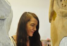 Elisabeth von Samsonow im „Göttinnenland“ Auf dem Bild sieht man Elisabeth von Samsonow von der Seite . Sie steht zwischen zwei Holzskulpturen