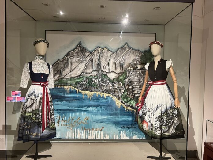 Das Bild zeigt die Ausstellungswerke von Sabine Linke Links und Rechts eine Puppe im Dirndl mit schöner handbemalter Schürze. In der Mitte im Hintergrund ein gemaltes Bild von Hallstatt,
