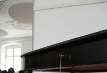 Looted: Two Families, Nazi Theft and the Search for Restitution / Kulturforum London Foto eines schwarzen Holztisches mit Ornamenten an den Tischbeinen auf einem Holzboden mit einem Spiegel im Hintergrund.