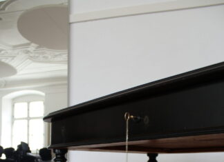 Looted: Two Families, Nazi Theft and the Search for Restitution / Kulturforum London Foto eines schwarzen Holztisches mit Ornamenten an den Tischbeinen auf einem Holzboden mit einem Spiegel im Hintergrund.