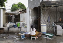 Fotografia Calabria Festival / Kulturforum Rom Das Bild zeigt eine im Friedhof von Metro Manila lebende Frau beim Wäsche waschen im Freien. Sie ist der Kamera mit dem Rücken zugewandt. Die Umgebung wirkt sehr heruntergekommen.