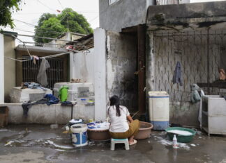 Fotografia Calabria Festival / Kulturforum Rom Das Bild zeigt eine im Friedhof von Metro Manila lebende Frau beim Wäsche waschen im Freien. Sie ist der Kamera mit dem Rücken zugewandt. Die Umgebung wirkt sehr heruntergekommen.