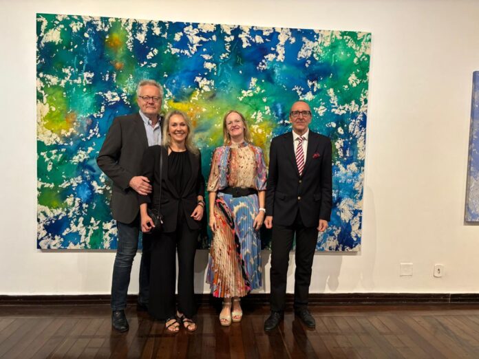 Bild: ÖB Brasilia Das Bild zeigt ein großformatiges abstraktes Kunstwerk in kräftigem Blau, Grün und Gelb und davor aufgestellt die Künstlerin Monika Kus-Picco mit Ehemann sowie Botschafter Dr. Stefan Scholz mit Ehefrau.