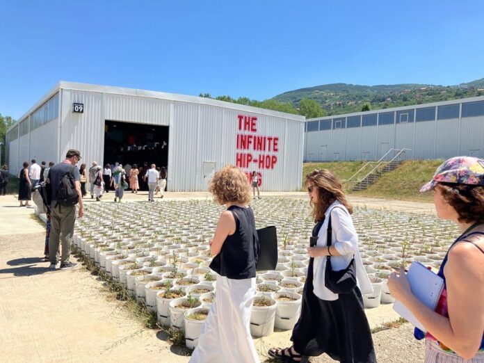 Bild: ÖB Pristina Das Bild zeigt Kunstwerk mit Blumentöpfen vor Hangar-Ausstellungsraum mit Aufschrift „The Infinite Hip-Hop Song“