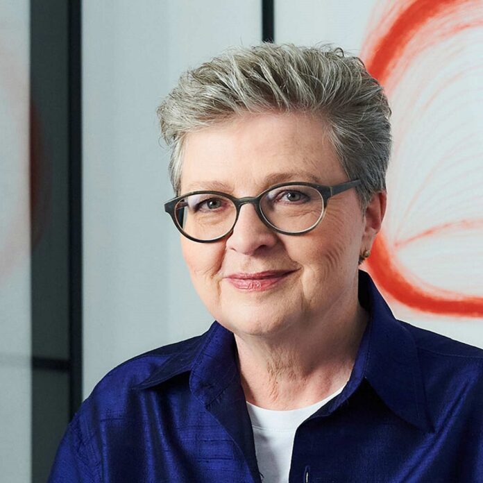 Podcast Auf dem Bild sieht man Hannah Rieger in Großaufnahme, sie trägt kurzes graues Haar und eine Brille und lächelt in die Kamera.