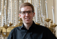 Internationales Orgelfestival Ligurien / Kulturforum Mailand Das Bild zeigt Peter Tiefengraber: er trägt ein schwarzes Hemd und schwarze Hose. Braune Haare mit Seitenscheitel, eine Brille, er steht aufrecht da und lächelt in die Kamera.