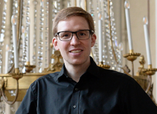 Internationales Orgelfestival Ligurien / Kulturforum Mailand Das Bild zeigt Peter Tiefengraber: er trägt ein schwarzes Hemd und schwarze Hose. Braune Haare mit Seitenscheitel, eine Brille, er steht aufrecht da und lächelt in die Kamera.