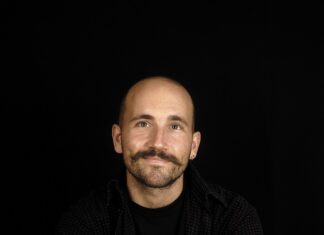 Flying Carpet Children Festival in Mardin / Kulturforum Istanbul Das Bild zeigt einen Mann mit Glatze und Schnurrbart vor schwarzem Hintergrund, der entspannt in die Kamera lächelt.