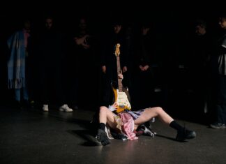 RAGE – Tanzperformance / Kulturforum Tel Aviv Das Bild zeigt die Tänzerin Daphna Horenczyk auf der Bühne liegend mit einer aufgestellten Gitarre.