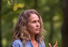 Fotografin Regina Hügli / Botschaft Tunis Das Bild zeigt Regina Hügli. Sie hat lange blonde Haare und trägt ein hellblaues Kleid. Sie gestikuliert erklärend mit den Händen und blickt nach rechts.