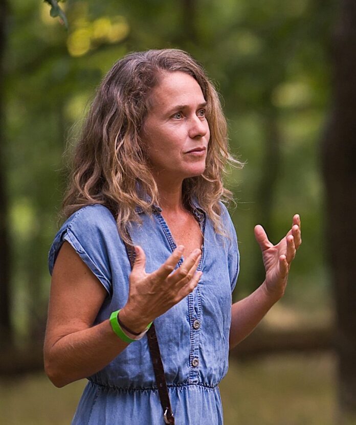 @Markus Bruckner Das Bild zeigt Regina Hügli. Sie hat lange blonde Haare und trägt ein hellblaues Kleid. Sie gestikuliert erklärend mit den Händen und blickt nach rechts.