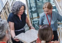 Netzwerktreffen der Österreich-Bibliotheken Es ist eine Frau in einer Bibliothek zu sehen, die vor sich eine grosse alte Urkunde aufgeschlagen hat und darauf blickt.