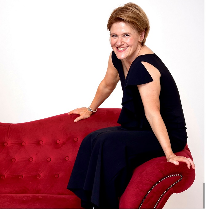 Bild: © Nicole Bernard Das Bild zeigt Pianistin Senka Brankovic, die auf der Lehne einer roten Couch sitzt. Sie trägt ein schwarzes Kleid und lächelt in die Kamera.