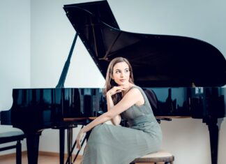 Pianorezital von Mitra Kotte / Kulturforum Istanbul und Botschaft Ankara Das Bild zeigt eine Frau in einem eleganten Kleid, die vor einem schwarzen Flügel sitzt und in die Ferne blickt.