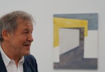 Closing: two dots one line / Kulturforum New York Ein älterer Mann mit grauen Haaren und heller Haut, bekleidet mit einem weißen Hemd und dunkelblauem Sakko, spricht gestikulierend. Er lächelt leicht und schaut nach links. Im Hintergrund hängt ein abstraktes Kunstwerk an der weißen Wand, bestehend aus geometrischen Formen in Gelb, Weiß und Blau. Im Vordergrund ist unscharf ein Teil einer weiteren Person zu sehen.