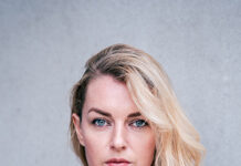 Valerie Fritsch / Botschaft Oslo Das Bild zeigt die Autorin Valerie Fritsch vor grauem Hintergrund. Sie trägt eine schwarzen Bluse mit V-Ausschnitt und schaut gerade in die Kamera. Sie hat blaue Augen und ihr schulterlanges blondes Haar trägt sie mit Seitenscheitel.