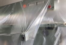 Veronika Eberhart: “Alles pelt zich” / Kulturforum Brüssel Das Bild zeigt eine Metallmaschine mit zwei roten Knöpfen, die mit durchsichtigem Kunststoff überzogen sind. Durch die Reflexion des Lichts auf dem Kunststoff ist es schwer zu erkennen, um welche Art von Maschine es sich handelt.