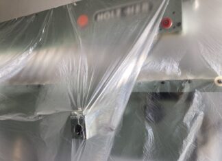 Veronika Eberhart: “Alles pelt zich” / Kulturforum Brüssel Das Bild zeigt eine Metallmaschine mit zwei roten Knöpfen, die mit durchsichtigem Kunststoff überzogen sind. Durch die Reflexion des Lichts auf dem Kunststoff ist es schwer zu erkennen, um welche Art von Maschine es sich handelt.