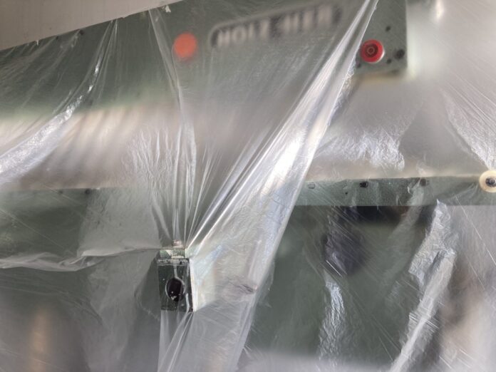 Das Bild zeigt eine Metallmaschine mit zwei roten Knöpfen, die mit durchsichtigem Kunststoff überzogen sind. Durch die Reflexion des Lichts auf dem Kunststoff ist es schwer zu erkennen, um welche Art von Maschine es sich handelt.