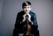 Feierliches Konzert / Kulturforum Zagreb Das Bild zeigt den jungen Geiger Leonhard Baumgartner. In seinen Händen hält er eine Violine, die senkrecht vor ihm steht, mit dem Griffbrett nach oben. Seine Hände sind an den Fingerspitzen zusammengelegt und ruhen auf dem oberen Ende der Violine.