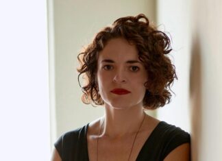 Lorena Moreno Vera / Botschaft Stockholm Das Bild zeigt die Kuratorin Lorena Moreno Vera. Sie hat kurze wellige dunkle Haare und trägt ein ärmelloses dunkles Kleid. Sie lehnt an einer Wand, hat die Hände vorne überkreuzt und blickt direkt in die Kamera.