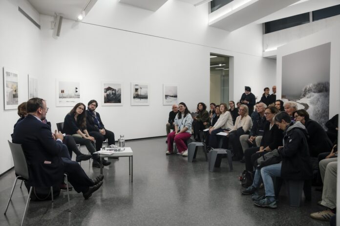 Bild: Buchpräsentation »Motherland hears, Motherland knows« von Dasha Karetnikova, FOTOHOF>EDITION 2025 Bilder: Anna Aicher / Isha Finian Martinez Crummer / Herman Seidl Das Bild zeigt vorne die Künstlerin, Herrn Staatssekretär Schellhorn, Frau Rabl-Stadler und noch einen Künstler, die miteinander sprechen. Davor das interessierte Publikum, sitzend, ca 30 Personen, an den Wänden die Fotografien.