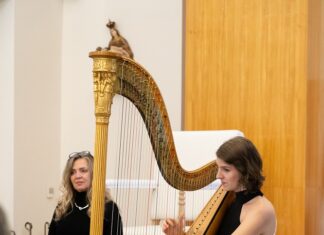 Harfenkonzert mit NASOM- Musikerin Elisabeth Plank / Kulturforum Bratislava Auf dem Bild ist die Musikerin auf der Harfe spielend zu sehen. Dahinter sitzt Beata Greneche mit einem Buch vor ihr.