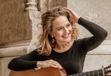 Rosa Franziska Maier in der Türkei / Kulturforum Istanbul Das Bild zeigt die österreichische Gitarristin Rosa Franziska Maier mit der Gitarre in der Hand. Sie hat langes blondes Haar, trägt ein grünes Shirt und einen bunten Rock. Mit einer Hand streicht sie sich die Haare zurück, mit der anderen hält sie die Gitarre auf ihrem Oberschenkel, sie lacht.