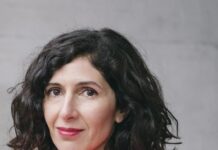 Nava Ebrahimi / Kulturforum Tokio Ein Porträt von Nava Ebrahimi. Sie hat schulterlanges schwarzes Haar und trägt einen rosaroten Rollkragenpullover. Sie blickt seitlich in die Kamera.