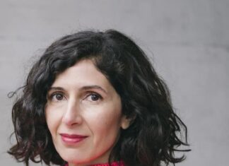 Nava Ebrahimi / Kulturforum Tokio Ein Porträt von Nava Ebrahimi. Sie hat schulterlanges schwarzes Haar und trägt einen rosaroten Rollkragenpullover. Sie blickt seitlich in die Kamera.