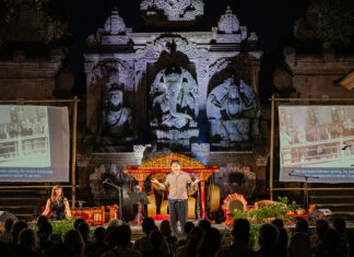 Empire – Rooting for the Antihero / Botschaft Jakarta Das Bild zeigt die Szene des Stücks in Ubud aus der Zuseherperspektive vor einer beeindruckenden javanischen Tempelkulisse. Im Zentrum ist der Schauspieler Marten Schmidt als Erzähler, links die Musikerin Anna Anderluh, rechts der Musiker Xinwei Thow und dahinter das Gamelan Orchester.