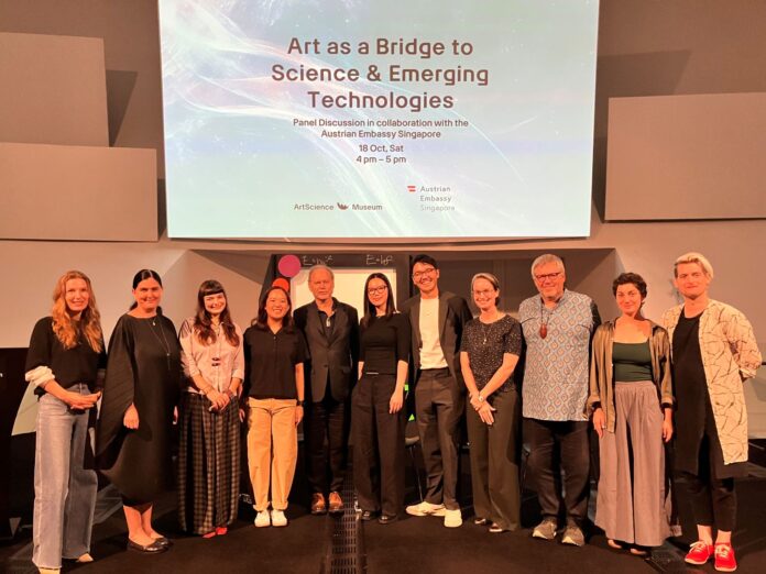 ÖB Singapur Das Bild zeigt vlnr Julia Henningsen (ÖB Singapur), Honor Harger (ArtScienceMuseum Singapore), Angelina Frank (Centre for Quantum Technologies), Debbie Gene Joseph (ArtScienceMuseum Singapore), Botschafter Peter Storer (ÖB Singapur), Chok Si Xuan (Installationskünstlerin), Mikhail Kennerley (PhD-Student NUS Singapore), Jenny Hogan (Centre for Quantum Technologies), Airan Berg, Alexandra Mayer-Pernkopf, Andreas Pfaffenberger (Zirkus d Wissens) vor dem Bildschirm im ArtSCiene Museum, der die Podiumsdiskussion ankündigt.