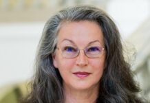 Leises Motto der Kultur-Diplomatie / Teresa Indjein Das Bild zeigt ein Portrait von Teresa Indjein. Sie trägt eine Brille und lange graue Haare, eine bunte Bluse mit einer grauen Jacke drüber. Sie blickt freundlich in die Kamera.