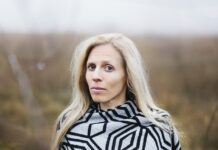 Sophie Reyer: Die Vielschreiberin / Podcast wissensArt Das Bild zeigt ein Portrait von Sophie Reyer. Sie steht in einer Landschaft, die verschwommen im Hintergrund sichtbar ist. Sie hat lange blonde Haare und blickt aufmerksam in die Kamera.