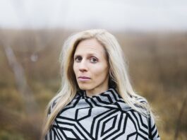 Sophie Reyer: Die Vielschreiberin / Podcast wissensArt Das Bild zeigt ein Portrait von Sophie Reyer. Sie steht in einer Landschaft, die verschwommen im Hintergrund sichtbar ist. Sie hat lange blonde Haare und blickt aufmerksam in die Kamera.